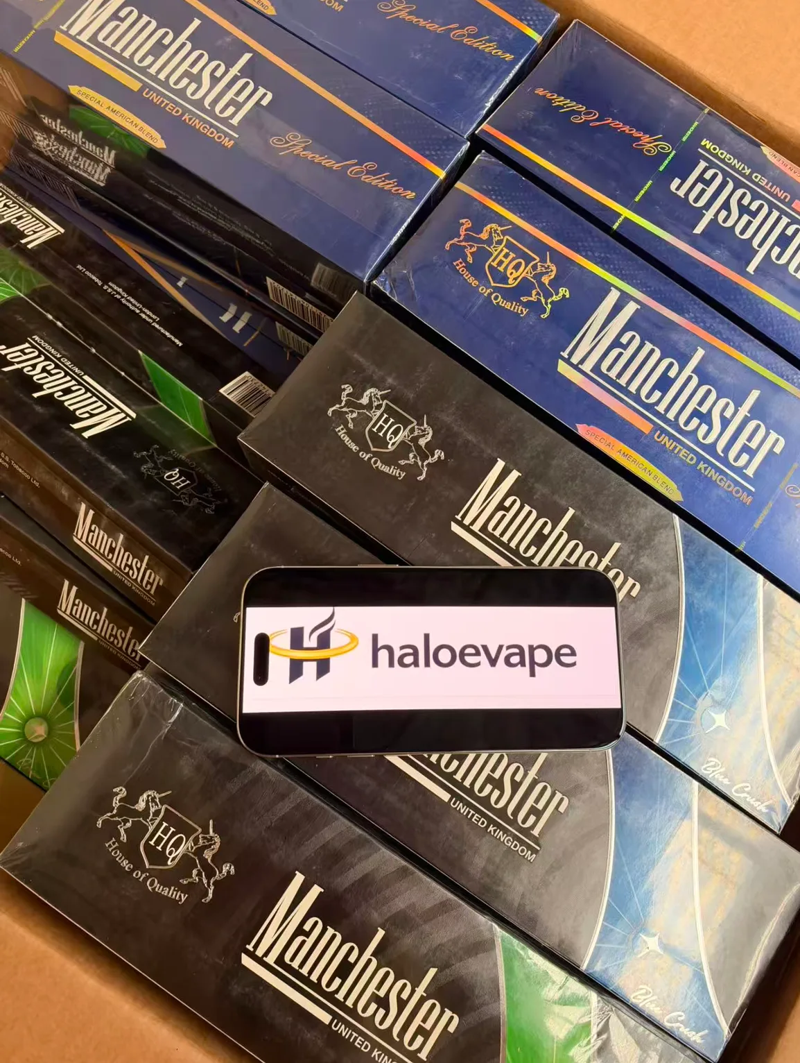 Manchester cigarette packs stacked at Halo E-Vape Australian warehouse with haloevape.com on screen